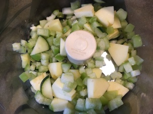 Half of the cucumber, apple, and tomatillos in a food processor.
